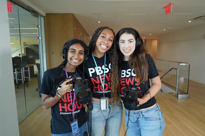 Fellows Navya, Sanaa and Miriam smiling for a photo in the WETA office holding cameras. 
