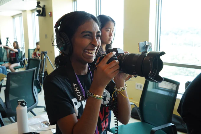 SRL Academy Summer Fellow Navya holding a camera with a headset on smiling 