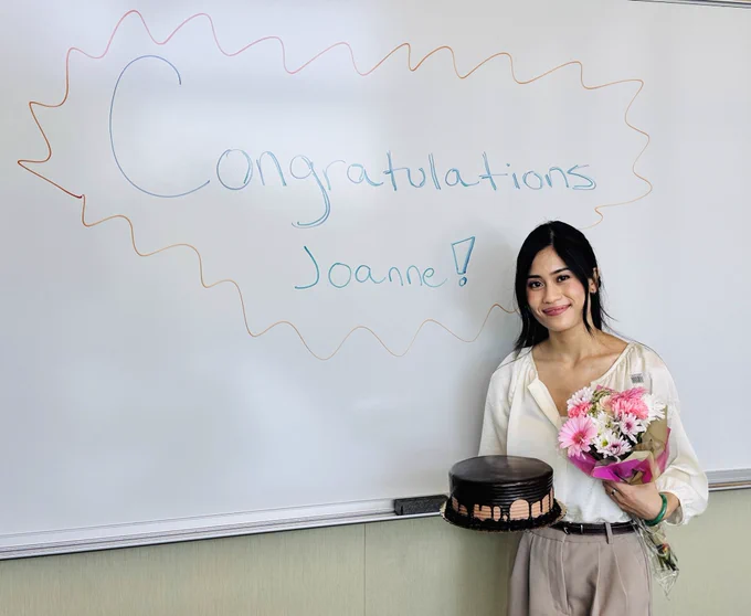 A picture of Joanne Mendez who is a new PhD candidate! She is standing in front of a white board and holding a yummy cake.