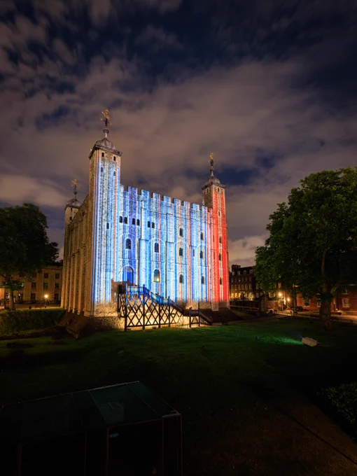 The White Tower at the Tower of London in the dark, lit up with stripes. On the left the stripes are blue, on the right they are red. 