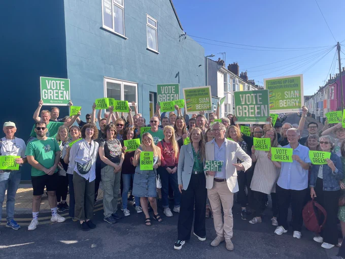Sian Berry and Steve Coogan with a large crowd of Greens in Hanover. Steve holding lego saying Elect Sian and many holding up signs saying Vote Green
