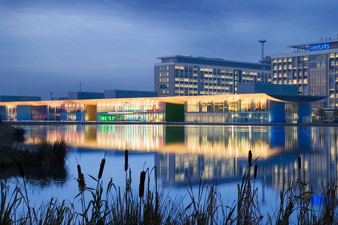 A wide shot of the High Tech Campus Eindhoven with moody lighting in the near-evening with water in front of the buildings.