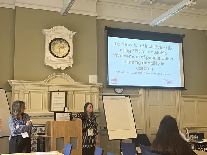 Amy Russell and Liz Croot stand at the front of a room giving a talk. The room is fancy it’s in Oxford and has a big clock.