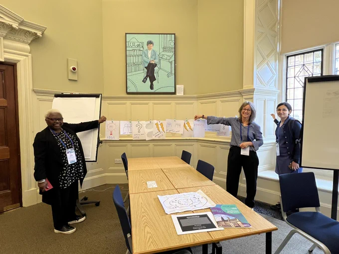 An example of a washing line exercise to plot a journey or story. Liz and Shoba and a colleague hold up a washing line of paper plotting a research journey.