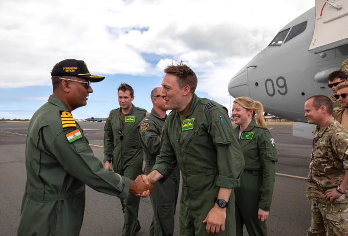 Image shows two men shaking hands with colleagues in the background.