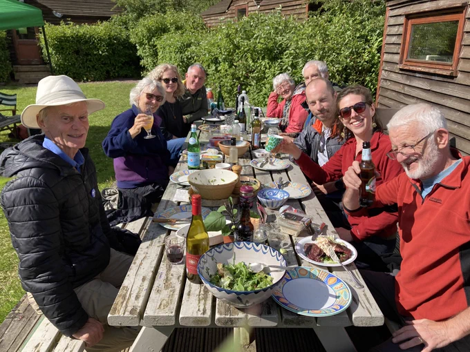 A group of people sitting around a table outside with food & drink.