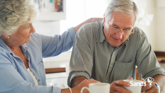 Image of older man and woman sitting talking at a table over a cup of tea.