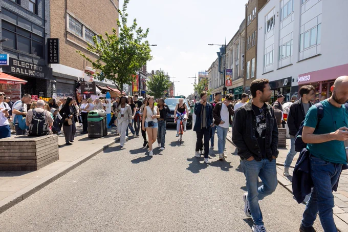 People walking in the carriageway of Camden High Street with traffic closely behind them.