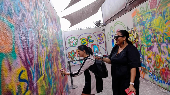Two people spray paint a wall.