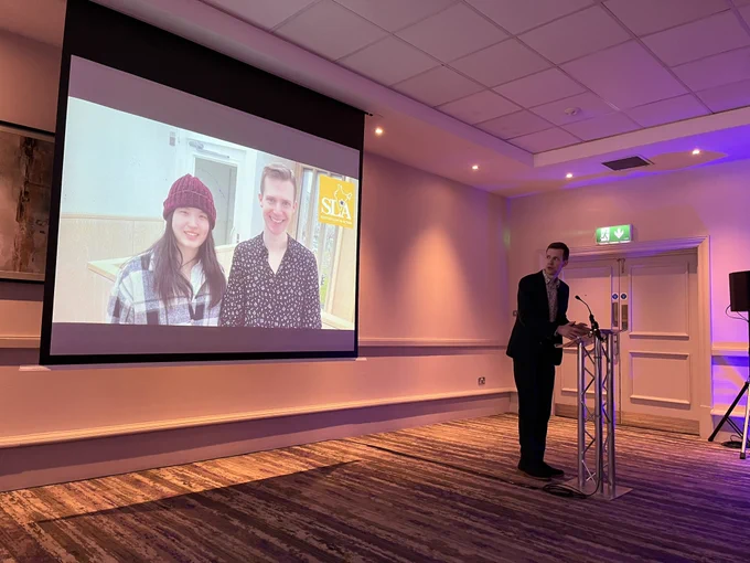 Jamie McIntosh at a lectern with a screen behind.