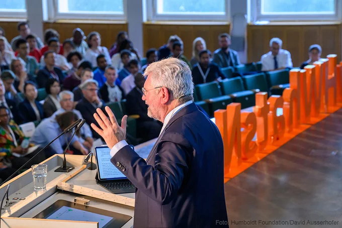 A man (Robert Schlögl) is holding a speech in front of an audience. 