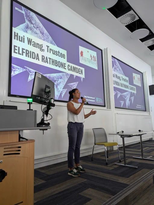 woman on stage speaking in front of presentation slide which says Hui Wang, Trustee, Elfrida Rathbone Camden