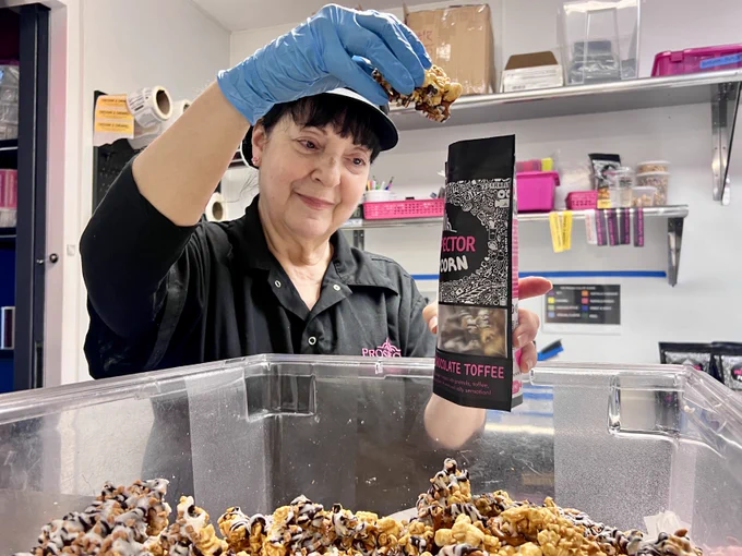 Connie adds more Belgian Chocolate Toffee gourmet popcorn to a bag in the kitchen.