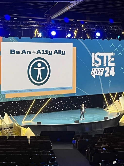 Katie standing in the stage in front of a slide that said Be an #A11y Ally