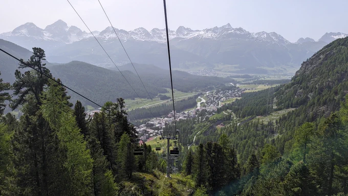 POV from a funicular, at the bottom the town, in the horizon the snowy moountains