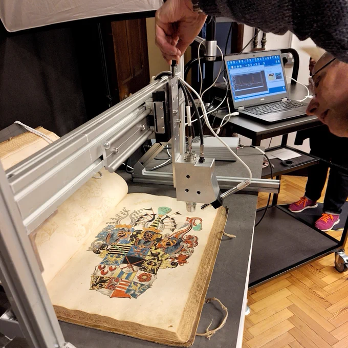 A colourful German Manuscript showing a large coat of arms under the ramen spectroscopy equipment. A computer shows the readout while a man adjusts the equipment.