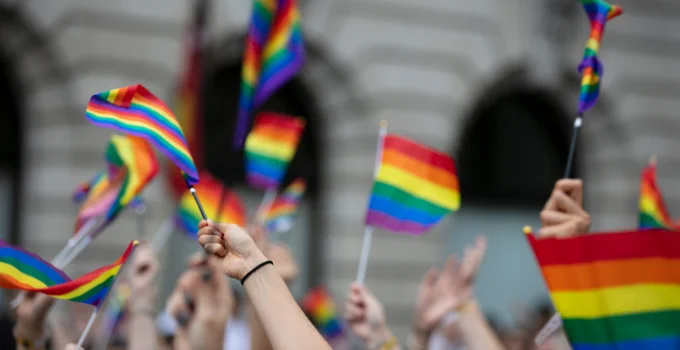 Rainbow Pride flags are held in the air. 