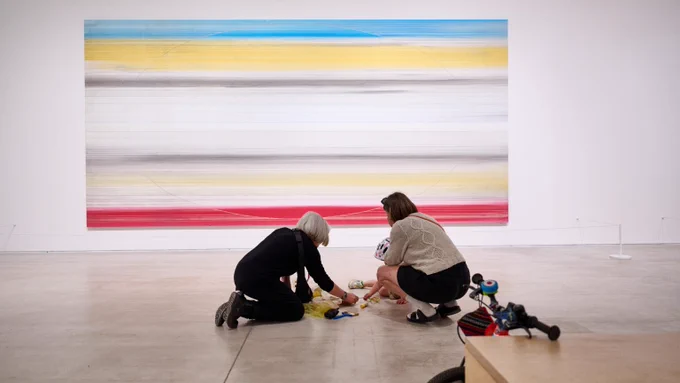 People play with a sensory activity in front of a piece of striped wall at at Turner Contemporary
