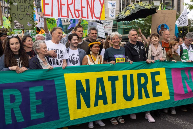 The front of a large protest, with a banner held by notable people including Chris Packam, Judi Dench, Emma Thompson and Dale Vince