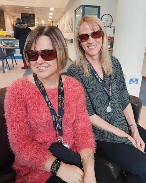 2 members of staff trying glasses on.