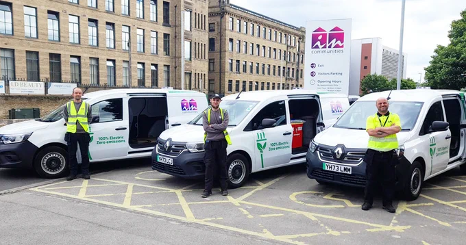 Three individuals in high-visibility vests stand by their parked vehicles.