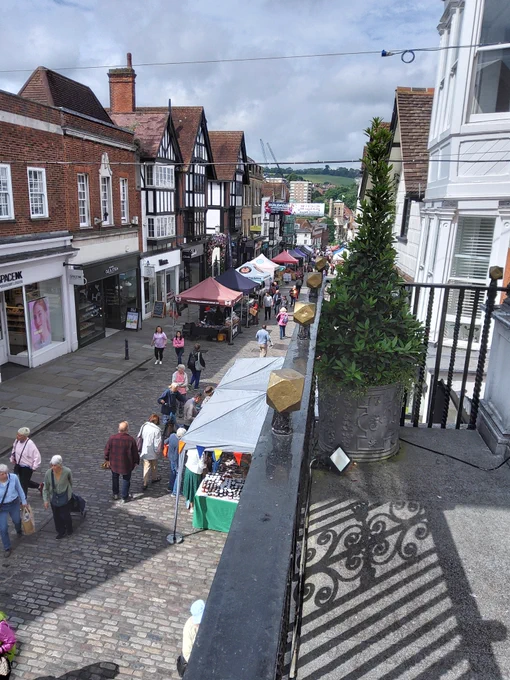 Colour photo taken from a balcony looking down a cobbled street with market stalls.