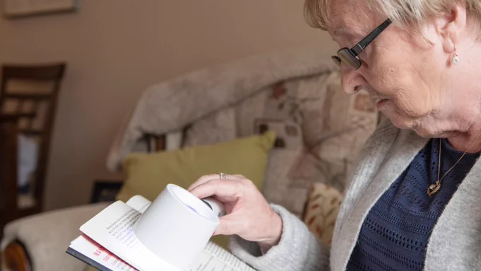 Older woman holding a magnifier and reading a letter. 