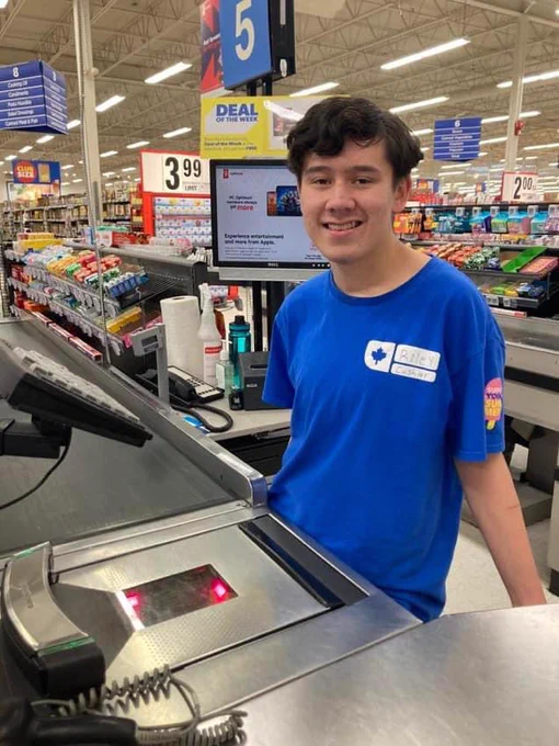 Photo of a person standing behind the till wearing their work uniform.