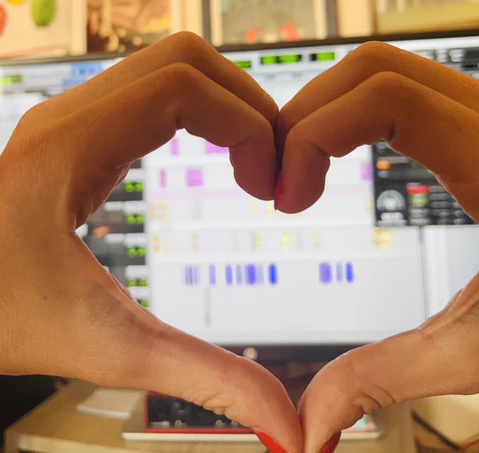 Becca’s hands forming a heart in front of a computer monitor displaying a pro tools session.
