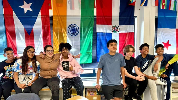 Smiling students sitting on a ledge in front of international flags.