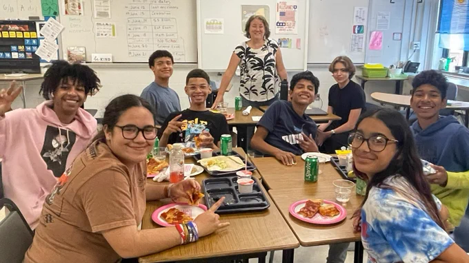 Smiling students sitting around desks enjoying celebratory snacks!