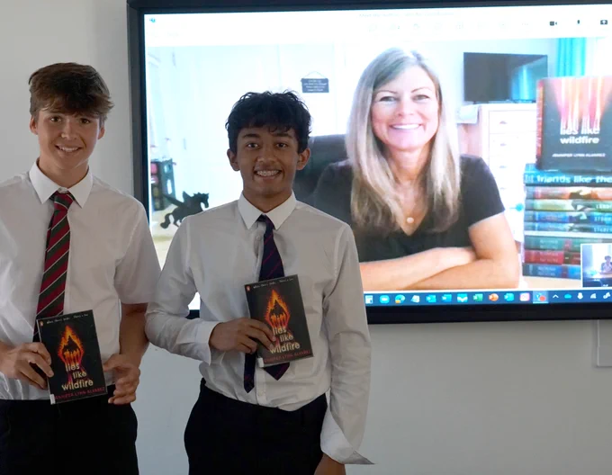 Two students holding books in front of a screen showing the author.