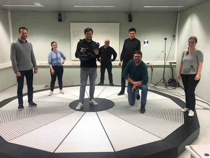 Seven researchers are standing on the surface of the omnidirectional treadmill and smile for the camera.