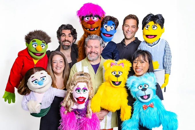 A photo showing a group of performers holding puppets and smiling together 