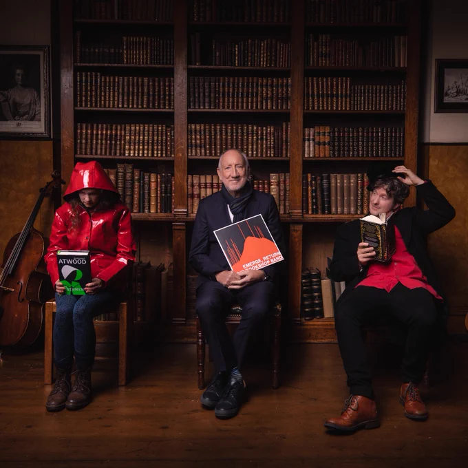 Pete Townshend flanked by Beth Porter and Ben Please of The Bookshop Band, by a wall of books holding a copy of their new album EMERGE RETURN.