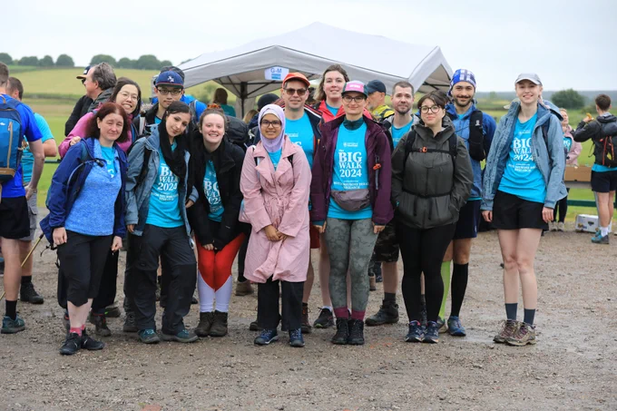 A group of people ready for a hike, smiling at the camera, hills and trees in distance