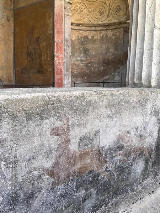 A dog chases a deer(?) through the greenery. Behind the colonnaded portico where the niche with the fresco of Menander seated and reading his scroll.