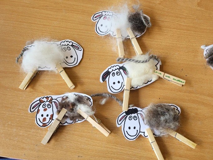 Cartoon sheep with legs made from clothes pegs.  Raw sheep's wool has been stuck to the body and more sheep's wool has been spun and twisted to form the tail.