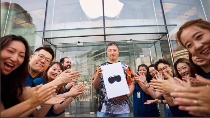 A customer holding up their Apple Vision Pro, surrounded by retail team members clapping.