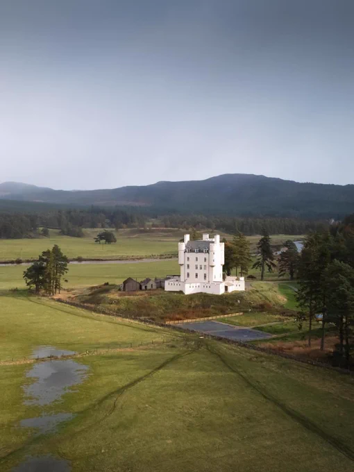 Image Description: A white castle on top of a grass-covered field with mountains in the background