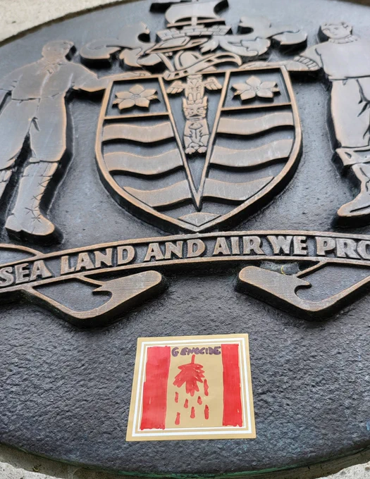 Upside down Canadian flag sticker saying genocide and dripping blood. On colonial plaque.