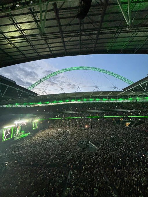 A picture taken during Green Day The Saviors Tour. The arch is lit up in green and a packed Wembley stadium can be seen.