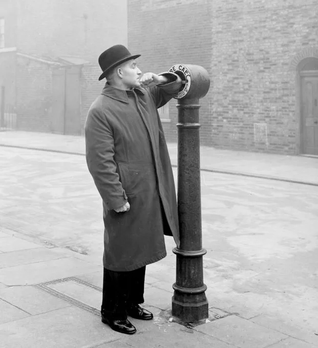 A man is demonstrating how to activate a street fire alarm by breaking the glass, taken in the 1930s