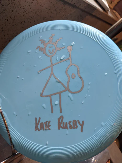 Photo of pale blue plastic Frisbee shaped like a shallow bowl with Kate Rusby written on it, along with a simple line art cartoon of her (bought at a gig many many years ago).
