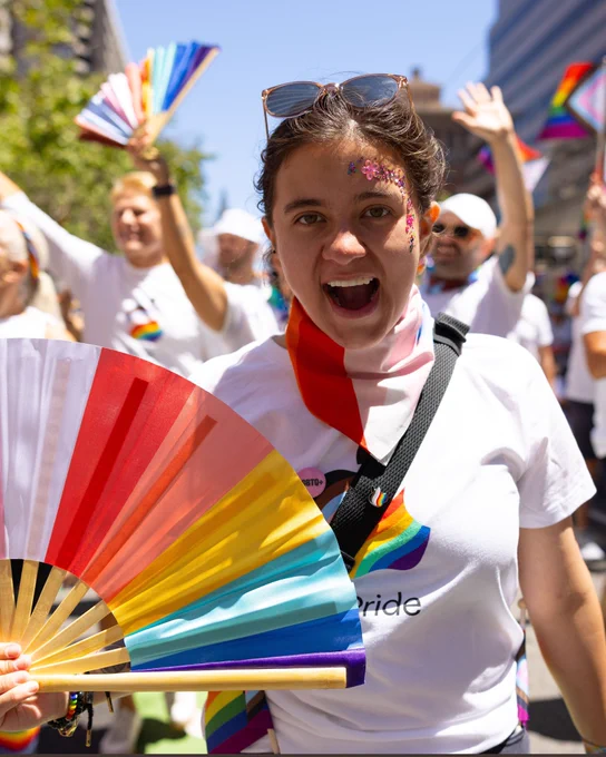 A team member waves a fan and cheers at the San Francisco Pride Parade.