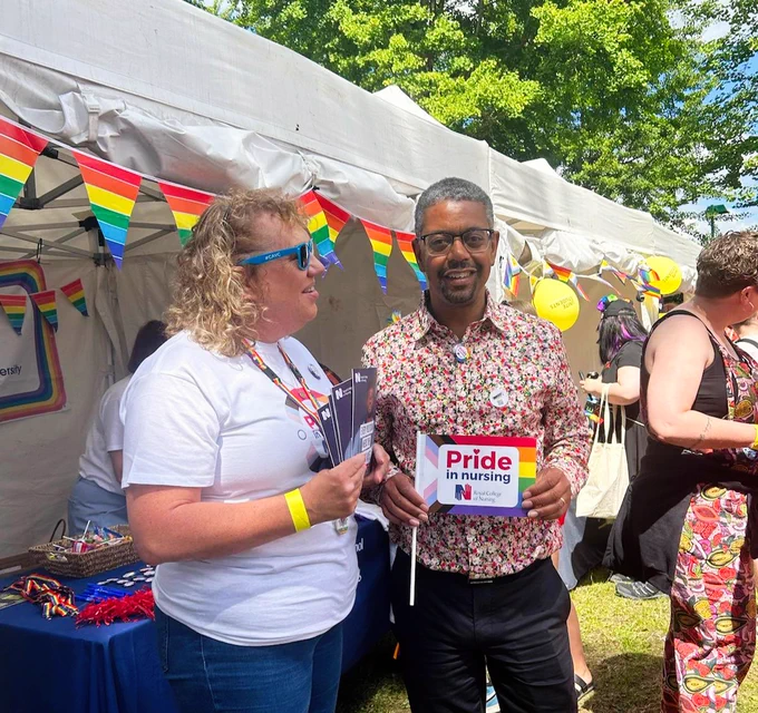 RCN members and staff standing under a tent decorated with colourful pride flags at an outdoor event. The person on the right is holding a sign that reads "Pride in Nursing." 