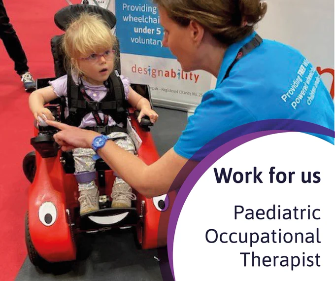 An occupational therapist crouched down beside a child trialling a Wizzybug powered wheelchair
