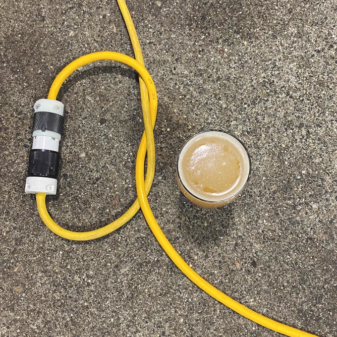 an arial view of a pint glass of beer on the concrete floor with two yellow electrical cords connected by large black and white plugs.
