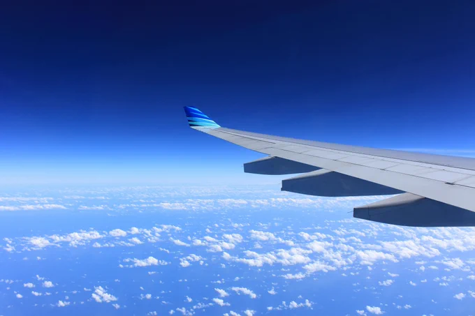 A gray airpane wing with a blue tip gliding over scattered clouds in a bright blue sky