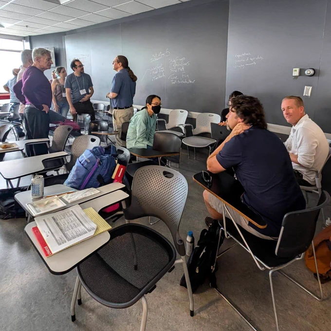 A group of 11 math educators in a Harvard classroom discussing the first day of a math modeling workshop.